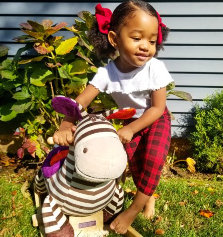 Smiling girl next to a rocking zebra toy.