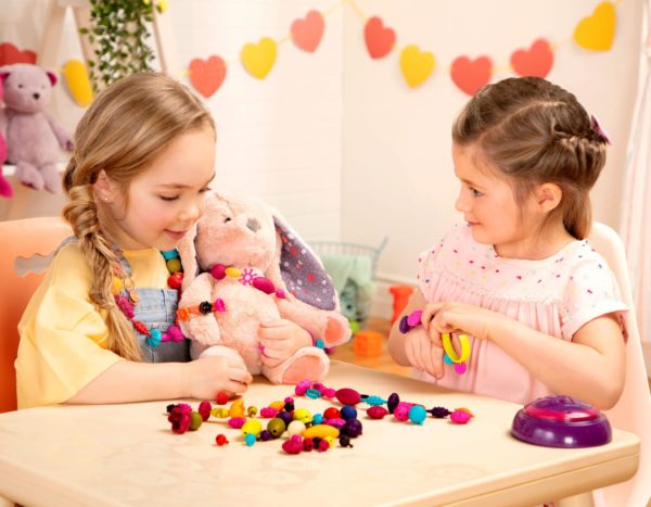 Two girls playing with snap-together jewelry while sitting at a kids table.
