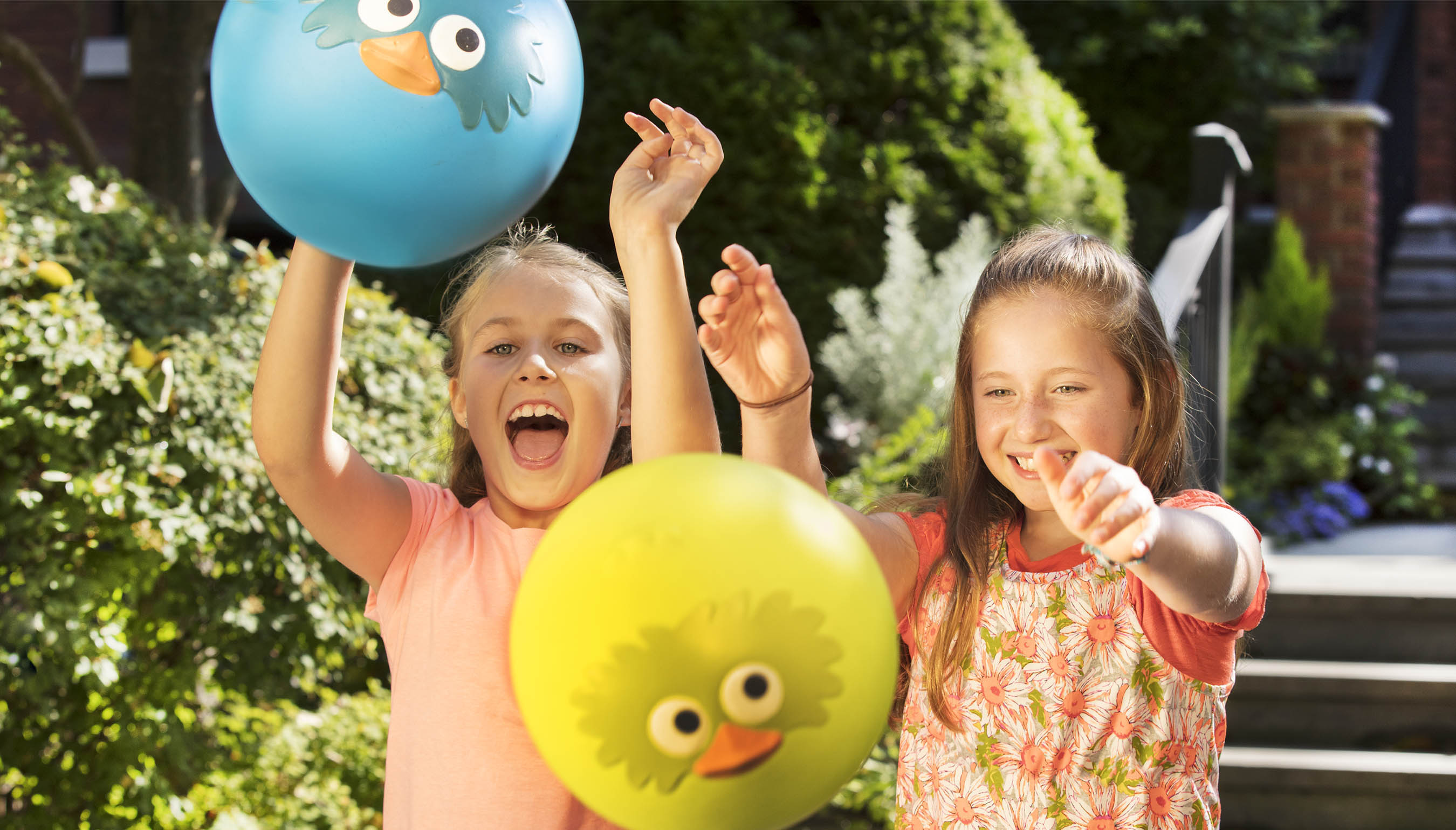 Dos niñas sonrientes jugando con pelotas hinchables inspiradas en pájaros.