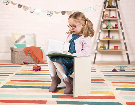 Girl reading a book on a step stool.